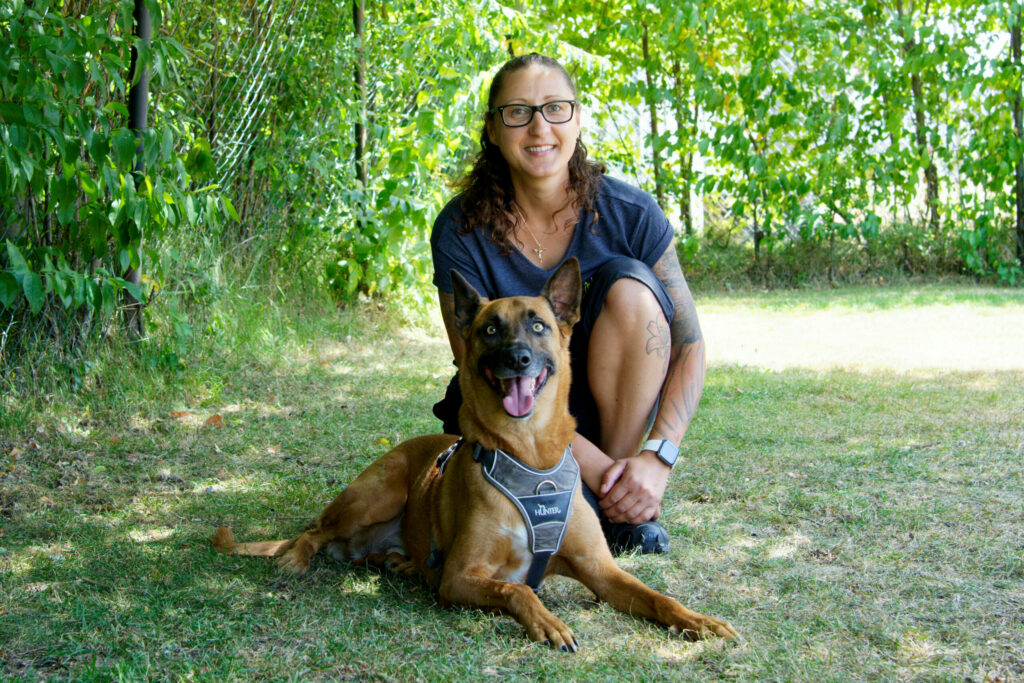 Hundetraining Franken - Team, Trainerin mit liegendem Malinois Rüde auf Wiese